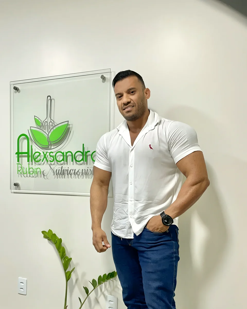 Alexsandro Rubin de camisa branca no consultório, em frente ao painel com seu logotipo